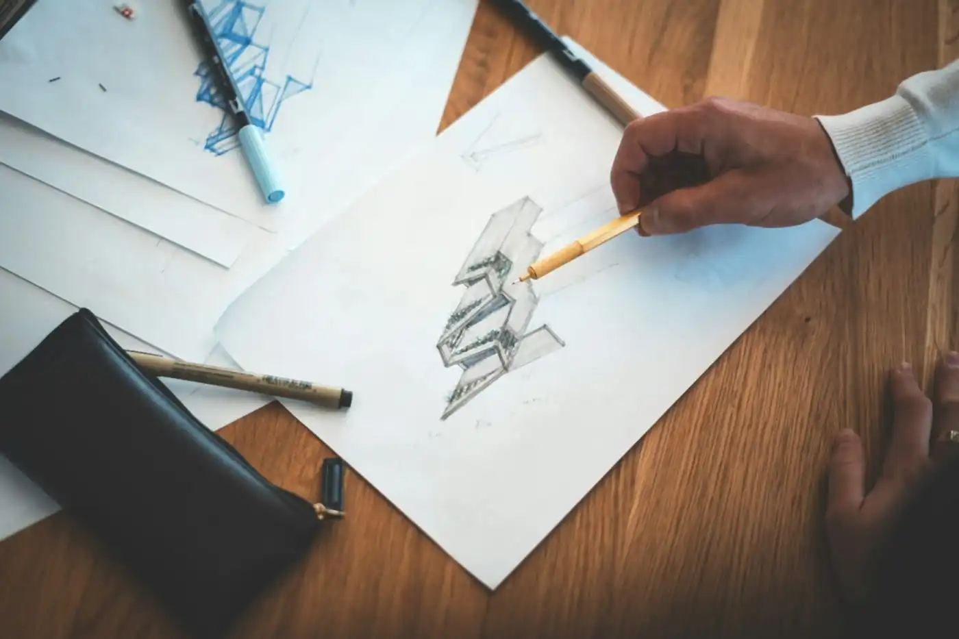 Hand sketching an interior design drawing with a fine pen on a wooden desk