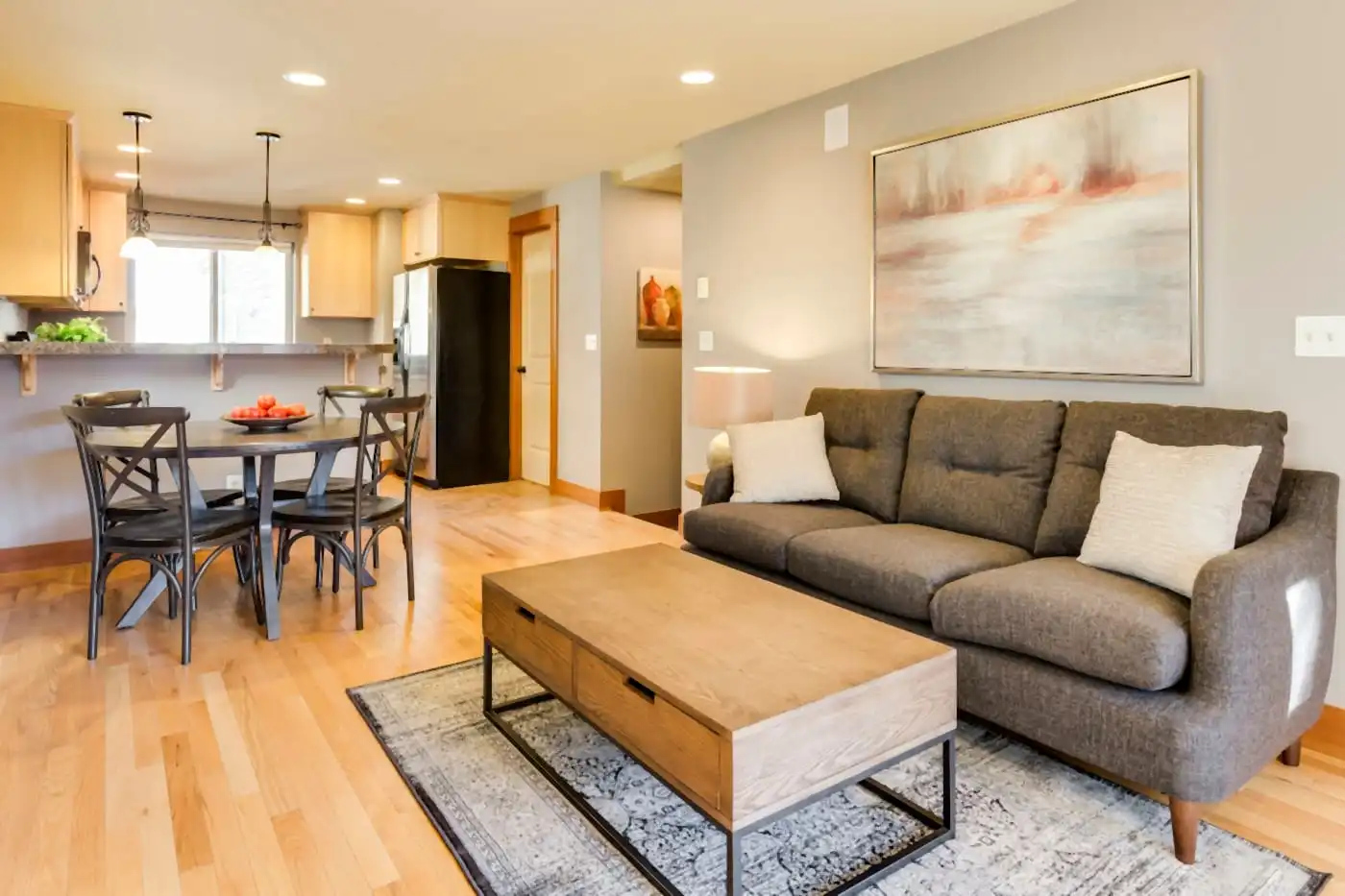 Open living and dining area with a sofa, coffee table and rug, and a dining table by the kitchen